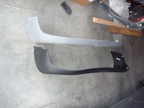 1997 Dodge 2500 - Two bumper covers, one gray and one black, are displayed on a concrete floor, possibly for sale or comparison.