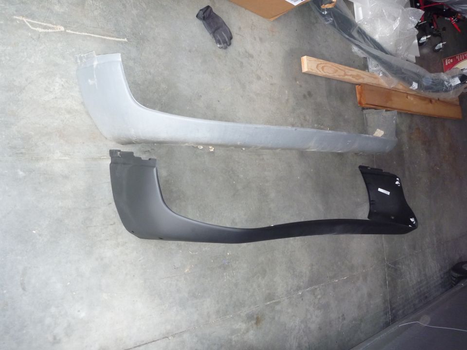 Two bumper covers, one gray and one black, laid out on a concrete floor