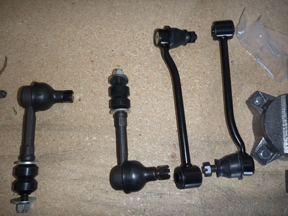 Several black suspension linkage parts laid out on a tan surface. Includes tie rod ends and sway bar links