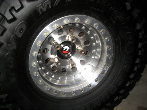 1996 Ford Bronco - A custom wheel with a black tire is shown, a prominent center cap with a red and white logo.