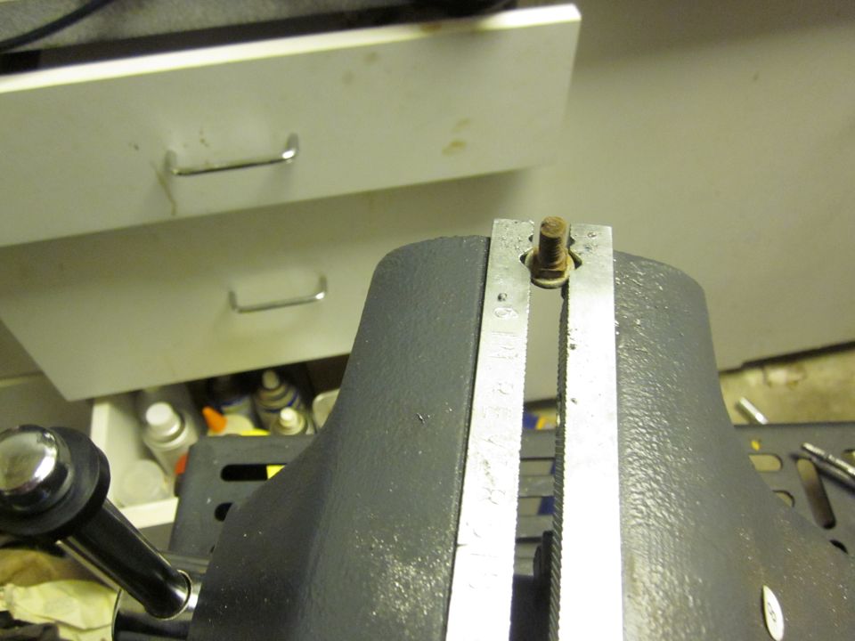 Close-up of a vise holding a bolt, with drawers in the background