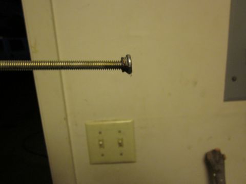 1979 Ford Bronco - A threaded rod with a nut is shown close up, with a light switch plate in the background.