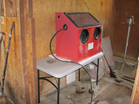 1979 Ford Bronco - A red sandblaster cabinet sits on a folding table in a workshop setting, with various tools and parts visible in the background.