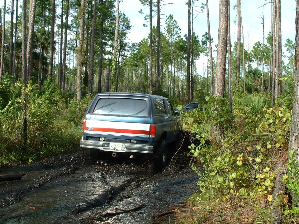 Blue and red Ford Bronco driving through mud in a forest
