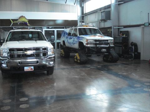 1979 Ford Bronco - A white Chevrolet pickup truck and a heavily modified SUV with tracks are parked inside a garage.