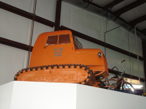 1979 Ford Bronco - An orange Tucker Sno-Cat vehicle is displayed indoors, with a bicycle visible to its right.