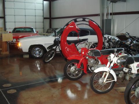 1979 Ford Bronco - A collection of vintage motorcycles and cars are displayed inside a garage, with a prominent red Honda motorcycle in the foreground.