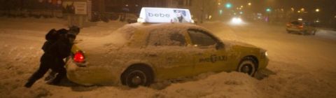2000 Ford Crown Victoria - A person attempts to push a yellow taxi out of deep snow on a city street at night.