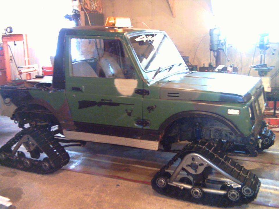 Camo Suzuki Samurai on rubber tracks instead of wheels, in a garage