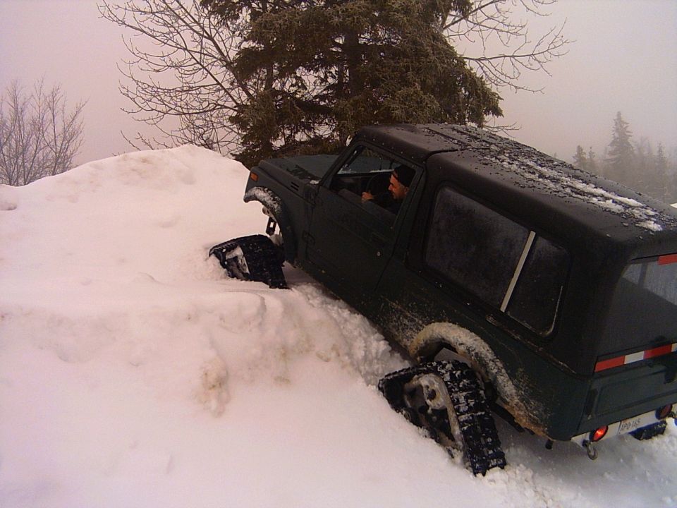 Dark green Suzuki Samurai hardtop stuck in deep snow, rear 3/4 view