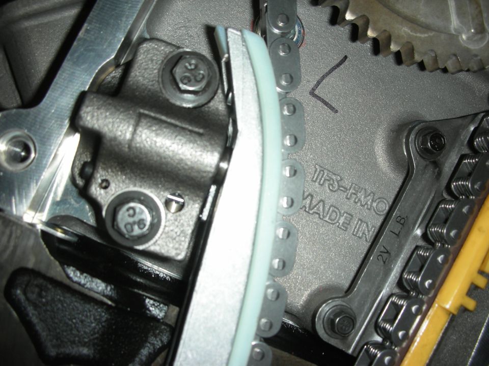 Close-up of engine timing chain, tensioner, and gears. "TFS-HMO MADE IN" is visible