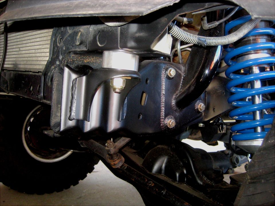Close-up of black metal suspension brackets and a blue coilover shock absorber on a vehicle