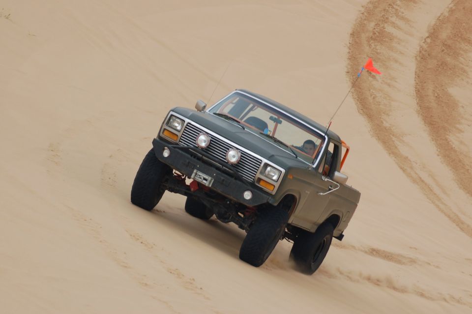 Dark green 1980 Ford Bronco off-roading on a sand dune