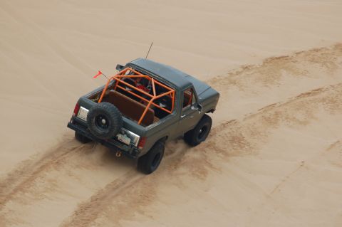 1982 Ford Bronco - A modified Ford Bronco navigates sandy terrain, its roll cage clearly visible.