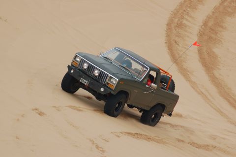 1982 Ford Bronco - This 1980s Ford Bronco navigates a sandy incline, equipped with an orange roll cage for off-road adventures.