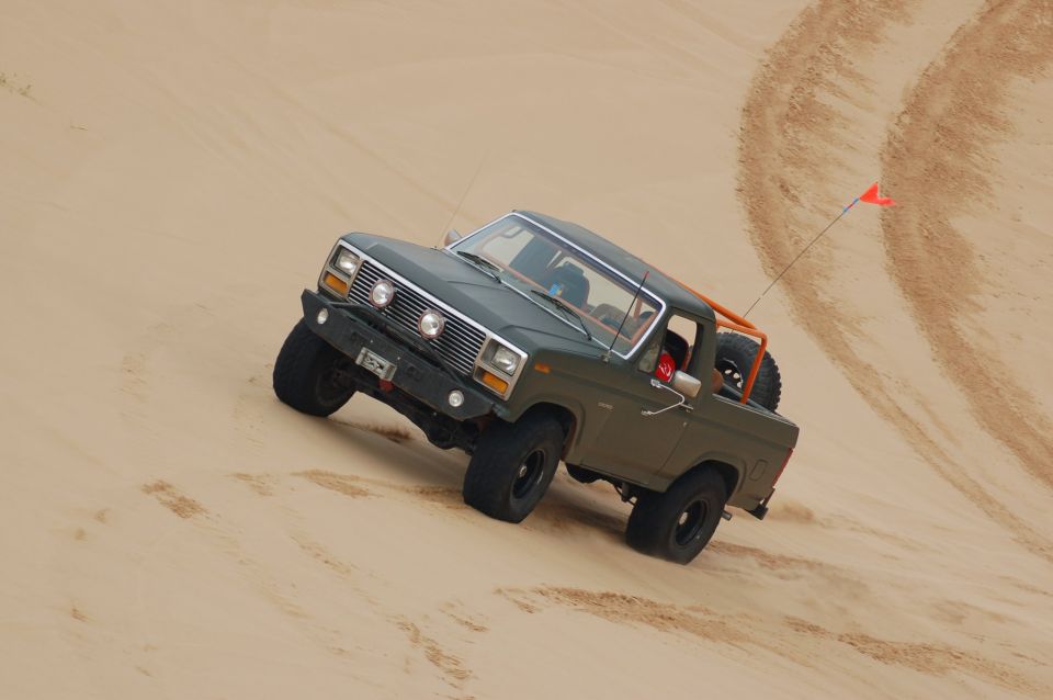 Green 1980s Ford Bronco climbing a sand dune with an orange roll cage