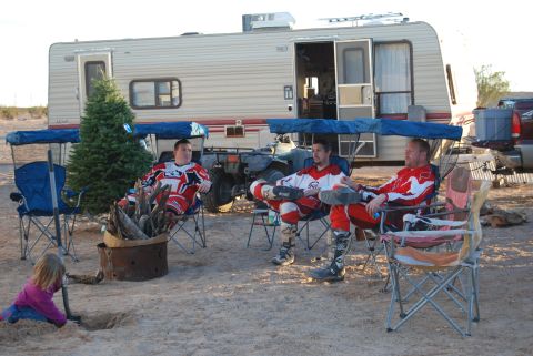 1982 Ford Bronco - Campers relax by a fire pit with a camper and ATV in the background.