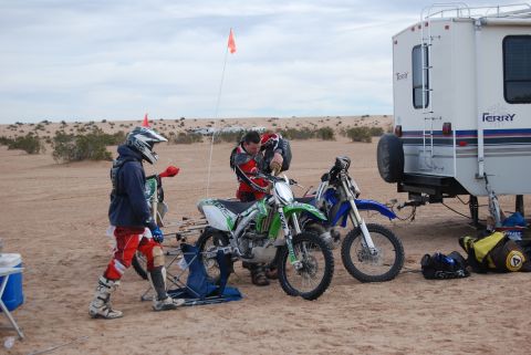 1982 Ford Bronco - Two dirt bikes are prepared for riding next to a white RV in a desert landscape.