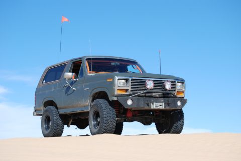 1982 Ford Bronco - A modified Ford Bronco sits on a sand dune under a clear blue sky.