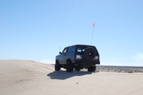 1982 Ford Bronco - This 1982 Ford Bronco is shown driving on sand dunes under a clear blue sky.
