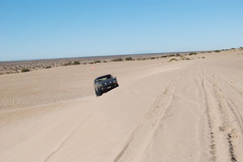 1982 Ford Bronco - A dark blue SUV navigates a sandy terrain under a clear blue sky.