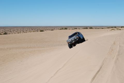1982 Ford Bronco - Ford Bronco navigates a sandy incline under a clear blue sky.