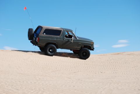 1982 Ford Bronco - This Ford Bronco is kicking up sand as it climbs a dune under a clear blue sky.