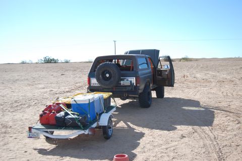 1982 Ford Bronco - SUV towing a trailer in a desert landscape. The vehicle's hood and driver's door are open.