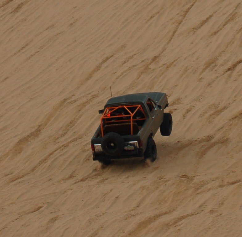 pickup truck with orange roll cage driving up a sand dune