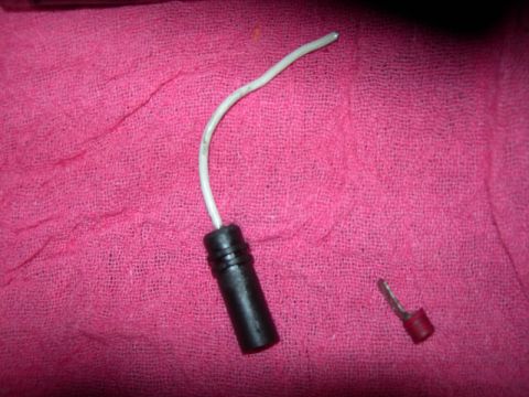 1984 Ford Bronco - A close-up of a detached electrical connector and wire, lying on a pink textured surface.