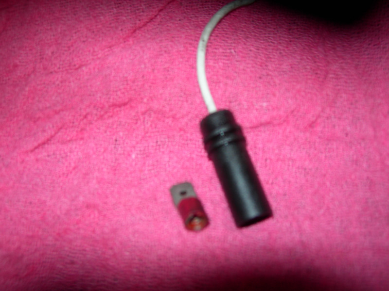 Black plastic connector with white wire and a small red and gray brake pad wear sensor on pink fabric