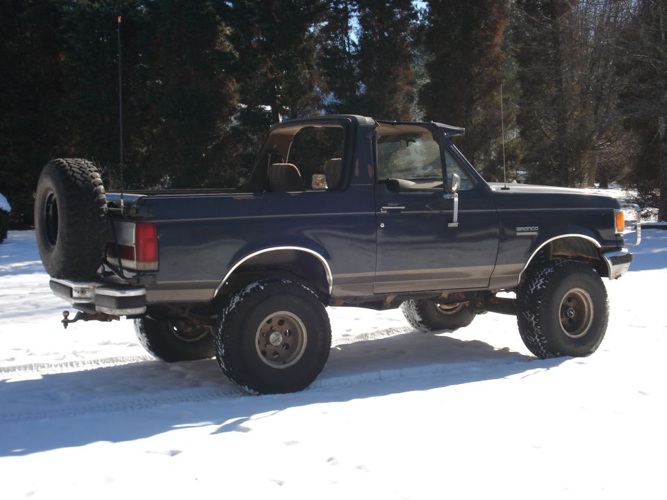 Dark blue 1988 Ford Bronco with removable roof and spare tire on back, parked in snow