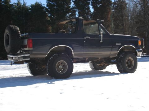 1988 Ford Bronco - Side view of a lifted Ford Bronco with its T-top removed, sitting in a snowy landscape.