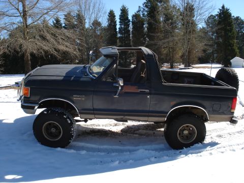 1988 Ford Bronco - A dark blue/black 1980s Ford Bronco shown in side profile with the top removed, sitting on a lifted suspension with large off-road tires an…
