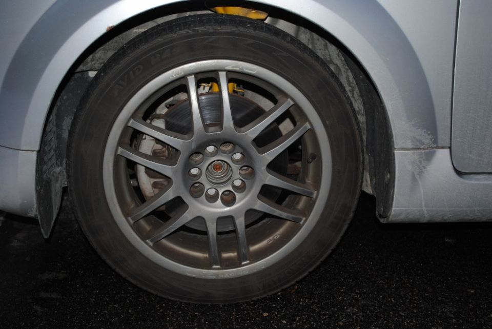 Silver multi-spoke alloy wheel and brake rotor on a dirty silver car