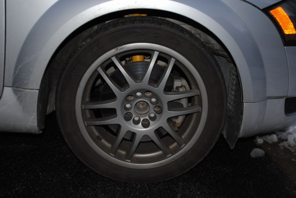 Silver alloy wheel with yellow spring visible behind spokes on a silver car