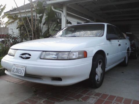 1992 Ford Taurus - A white 1992 Ford Taurus is parked in a driveway, showing its front 3/4 view with a California license plate.