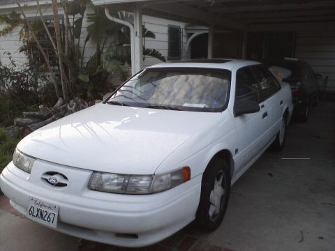 1992 Ford Taurus - This white 1992 Ford Taurus sedan is parked under a carport, with another vehicle visible behind it.