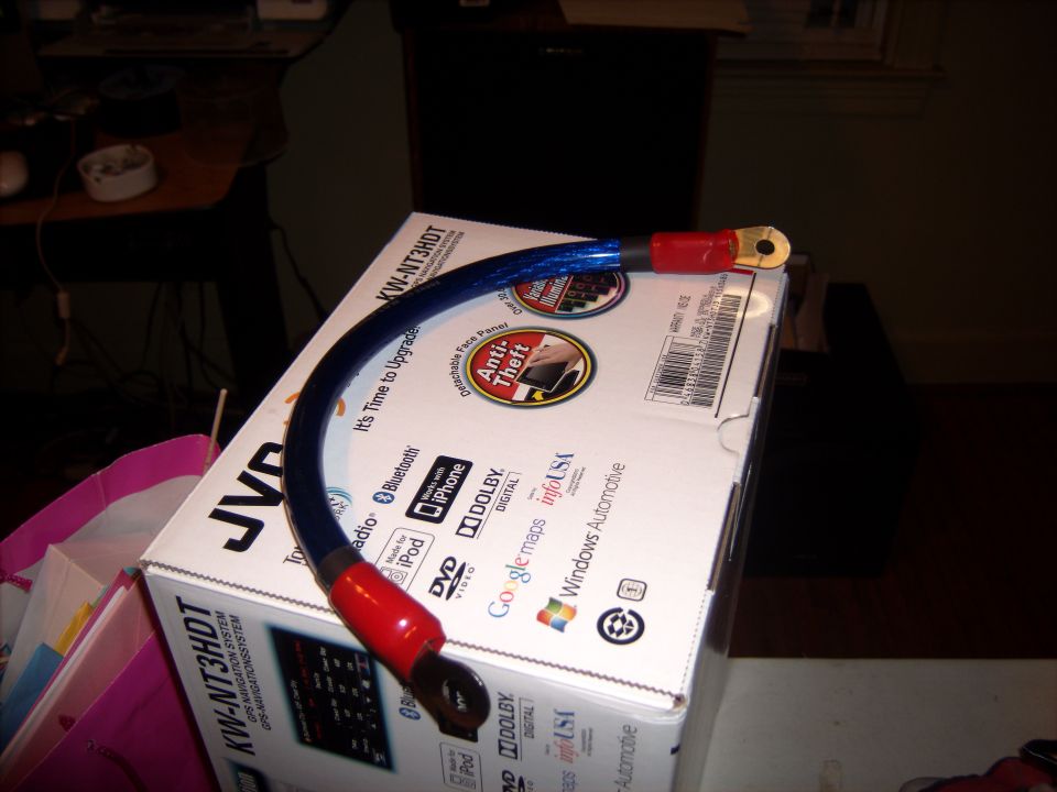 Blue battery cable with red ends and gold terminals sits on a JVC car stereo box