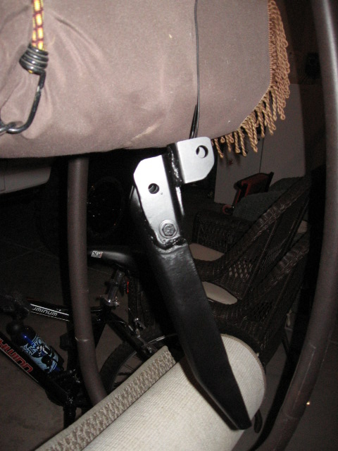 1995 Ford Bronco - A close-up view of a vehicle's shock mount bracket, with a bicycle and furniture in the background.