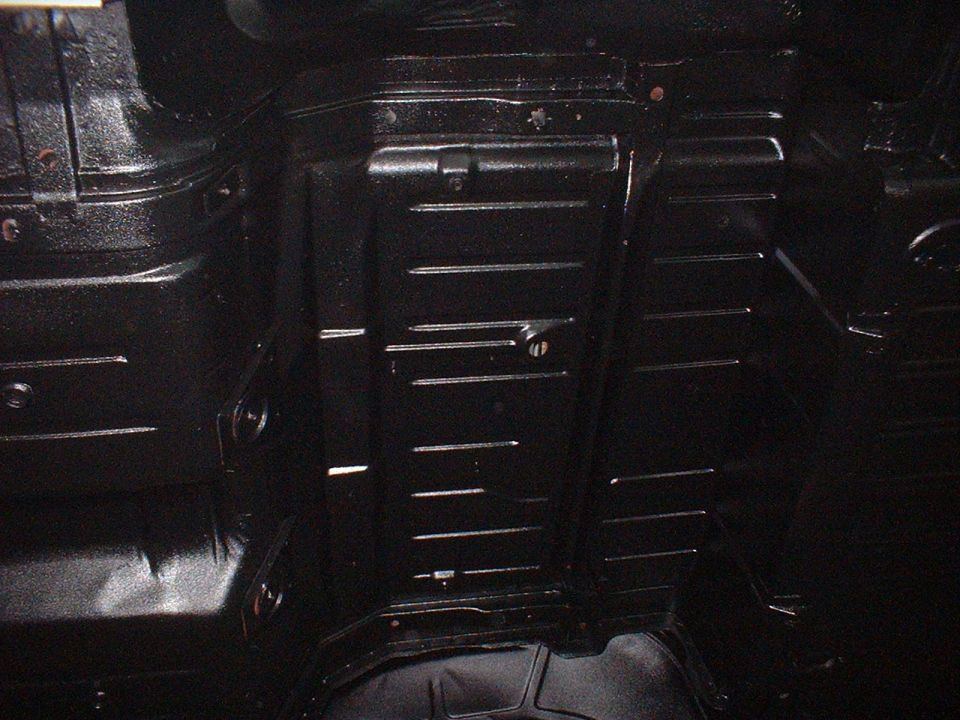 Underside of a car with black undercoating. Shows floor pan and frame components