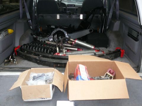 1988 Ford Bronco - Cargo area of a vehicle filled with suspension components and boxed parts, suggesting a project or repair.