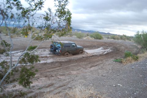1982 Ford Bronco - Ford Bronco navigating a muddy off-road course under a cloudy sky.