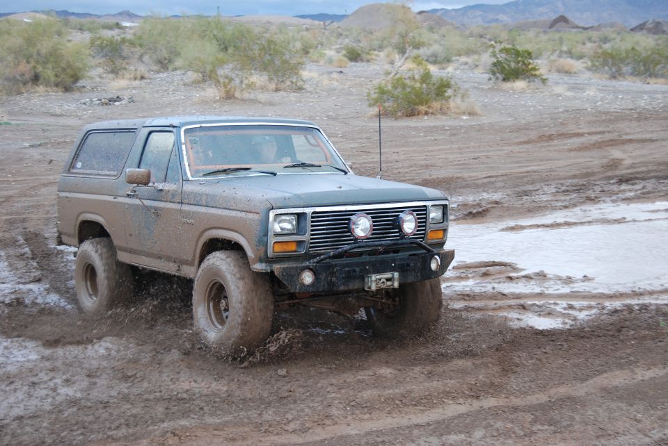 Muddy 1980 Ford Bronco driving through water and mud