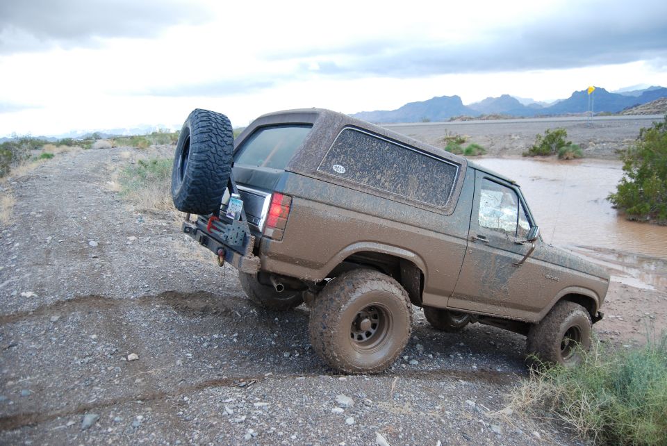 1982 Ford Bronco driving through muddy water, spare tire mounted on rear carrier