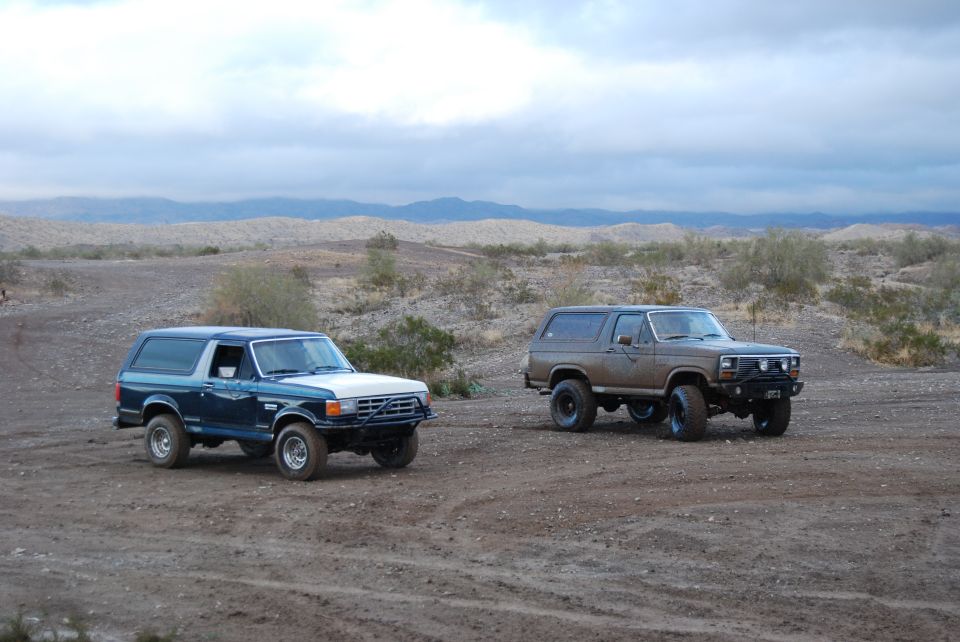 Two 1982 Ford Broncos parked in a desert with mountains in the background