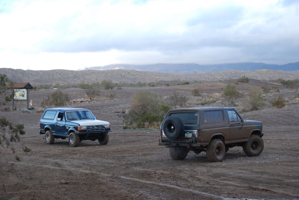 Brown Ford Bronco with spare tire on rear, blue Ford Bronco in background, desert scene
