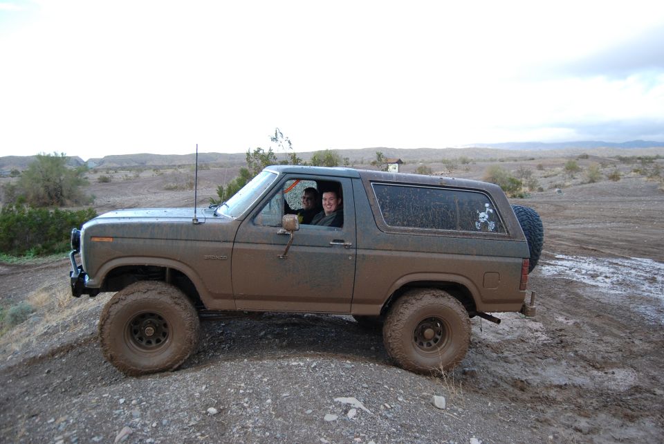 1982 Ford Bronco driving through mud with two people inside