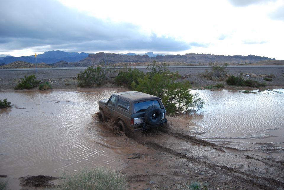 Ford Bronco driving through a muddy water puddle with mountains in the background