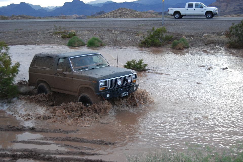 Brown 1982 Ford Bronco splashing through mud puddle
